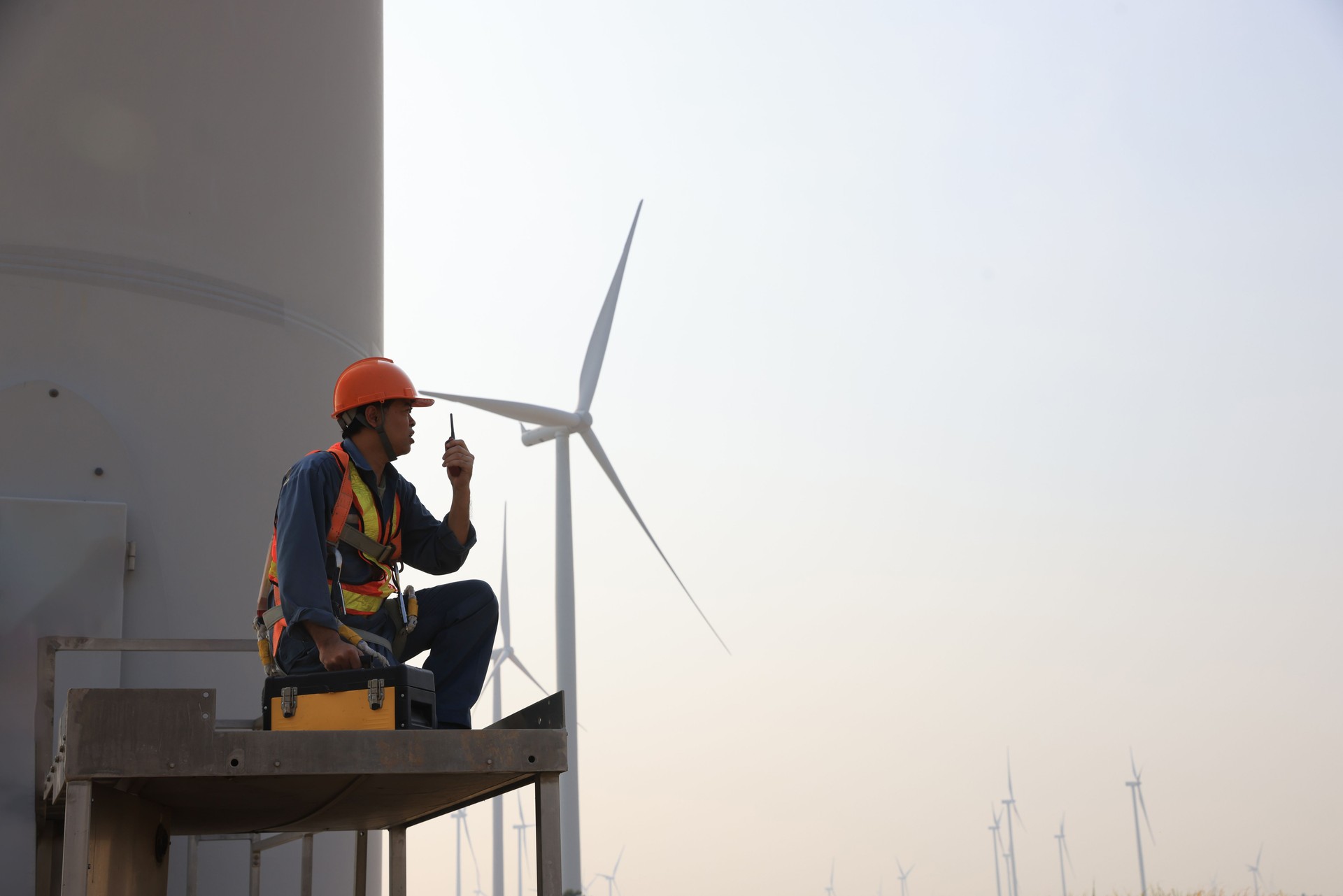 Specialist wind turbine technician working at the base of the turbine. Wind turbine service technician wearing safety uniform and safety harness working at windmill farm
